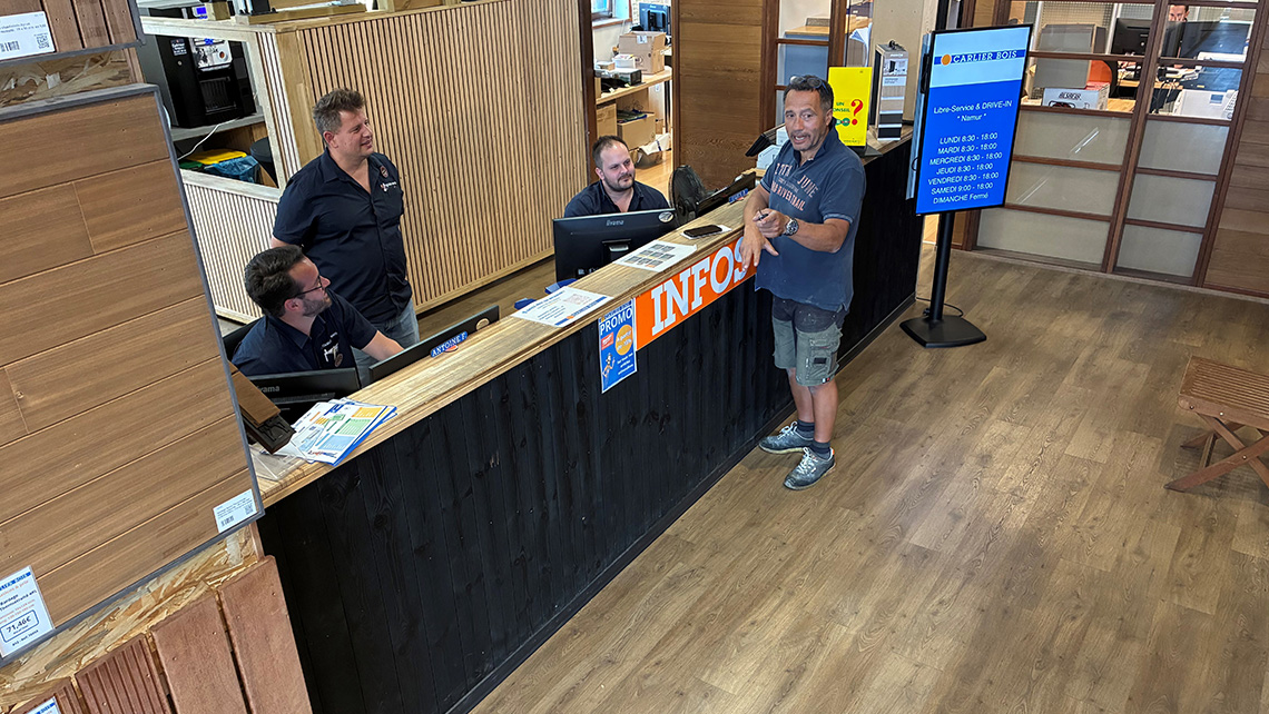 Un comptoir d'information à l'intérieur du magasin. Trois employés sont présents derrière le comptoir, l'un d'eux discutant avec un client. Le comptoir est marqué avec le mot 